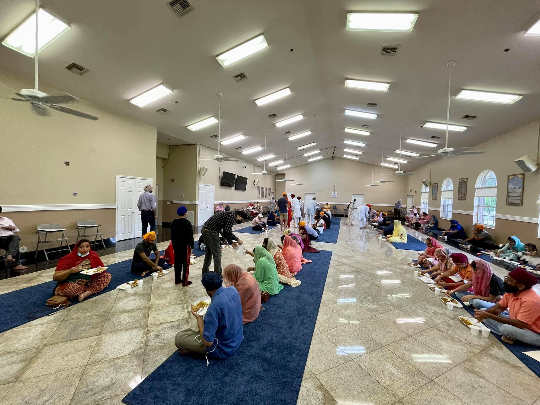 Sangat seated in rows sharing Langar