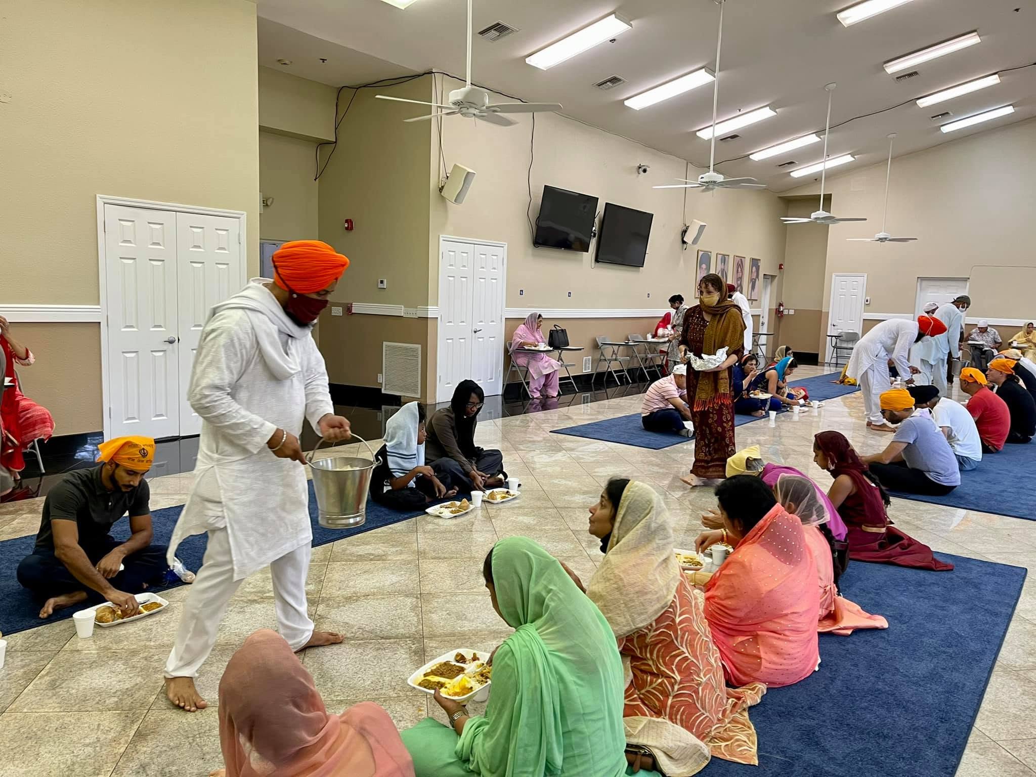 Volunteers serving Guru Ka Langar to the Sangat seated on the floor